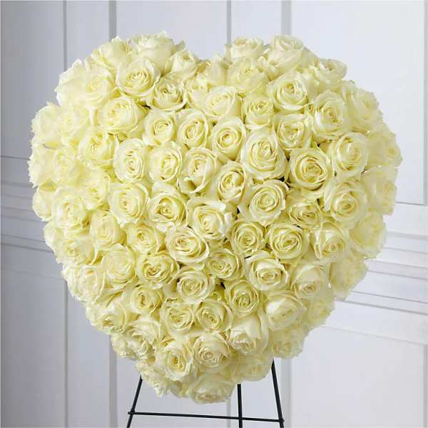 Heart-shaped arrangement of ivory roses displayed on a black metal easel.