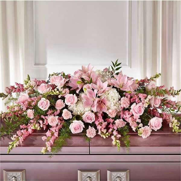 Pink and white casket spray with lilies, roses, carnations and trailing blooms on a closed casket.