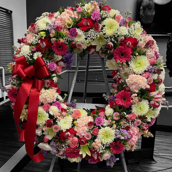Large standing wreath of pink, red, and white flowers with a red bow on an easel