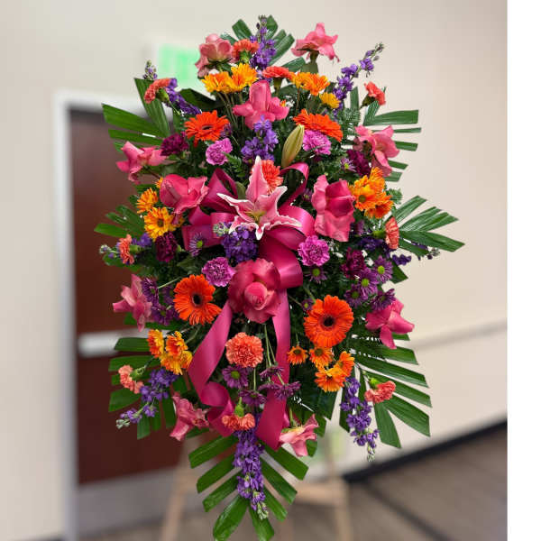 Tall standing spray of bright pink, orange, and purple flowers with a large pink bow