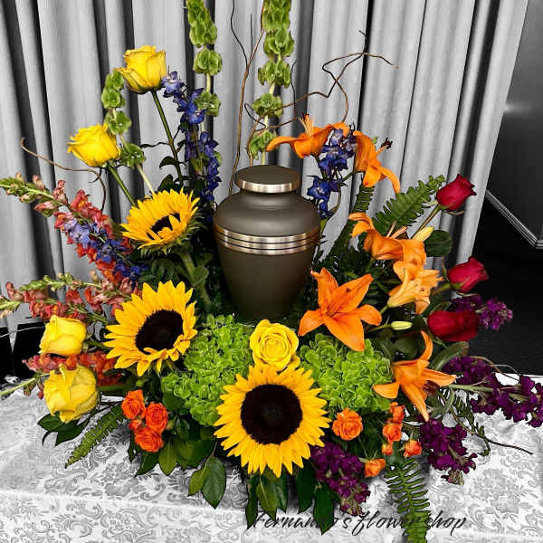 Cremation urn surrounded by bright sunflowers, lilies, roses, and mixed blooms on a table
