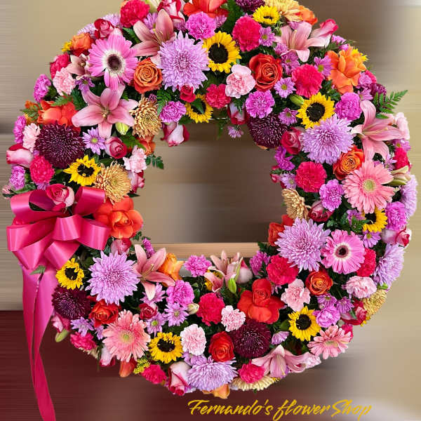 Bright circular wreath of mixed pink, yellow, and orange flowers with a large pink bow.