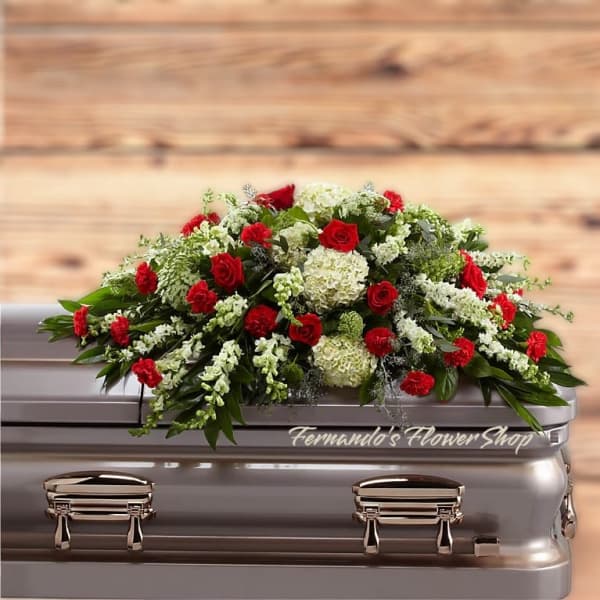 Red and white casket spray with roses, carnations, hydrangeas, and trailing white blooms on a silver casket