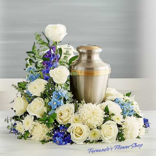 Cremation urn surrounded by white roses, white chrysanthemums, and blue flowers in a low arrangement