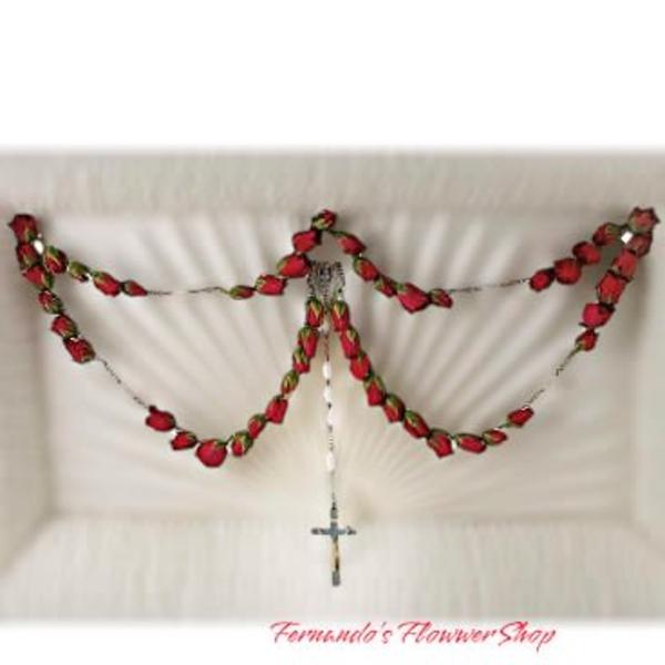 Red rosebud rosary garland with hanging cross draped inside a white casket lid