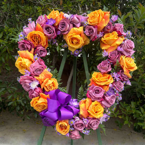 Heart-shaped rose wreath with purple ribbon on a stand
