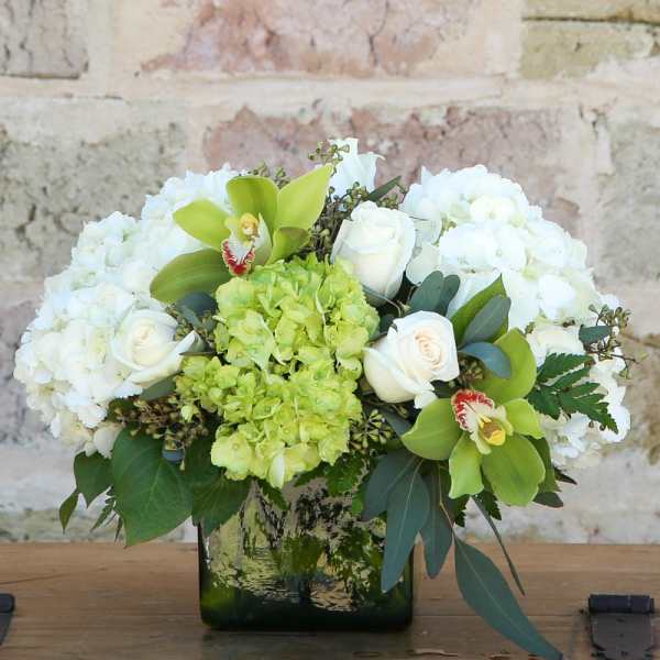 White roses and hydrangeas with green orchids in a glass vase