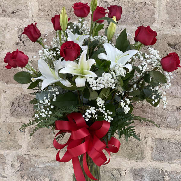 Red roses and white lilies in a clear glass vase with a red ribbon