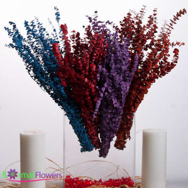 Tall multicolored floral arrangement in a clear vase with two white candles