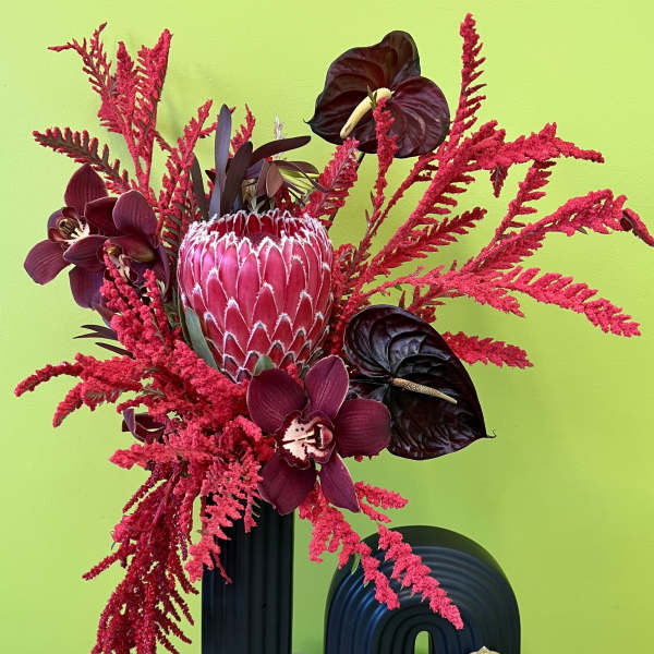 Bold red floral arrangement with orchids and a protea in a black vase