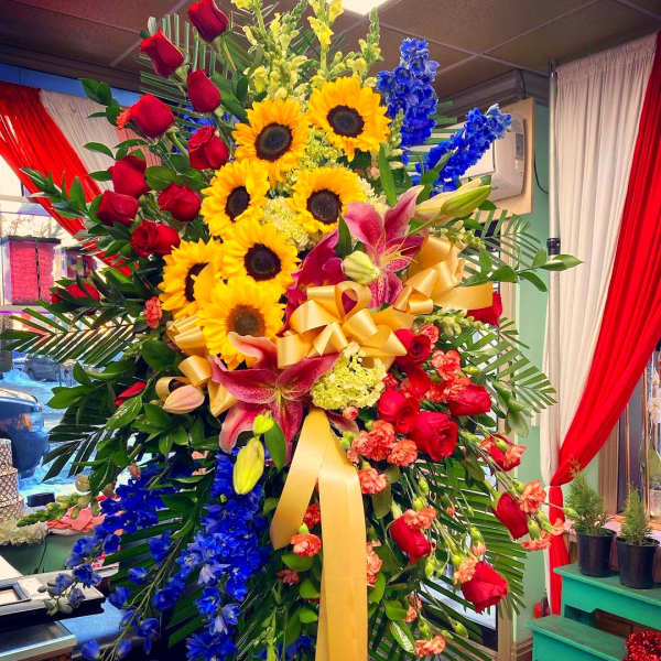 Large standing floral spray with sunflowers, red roses, and blue flowers
