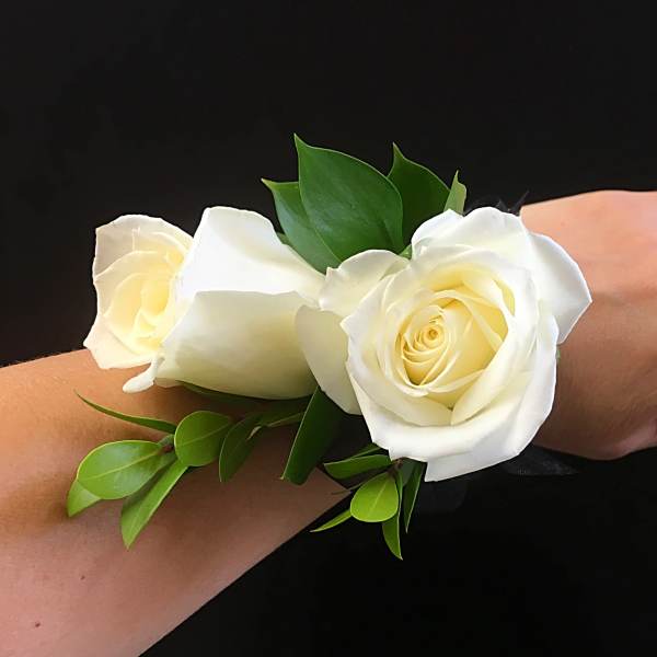 White rose wrist corsage with green leaves on a black ribbon