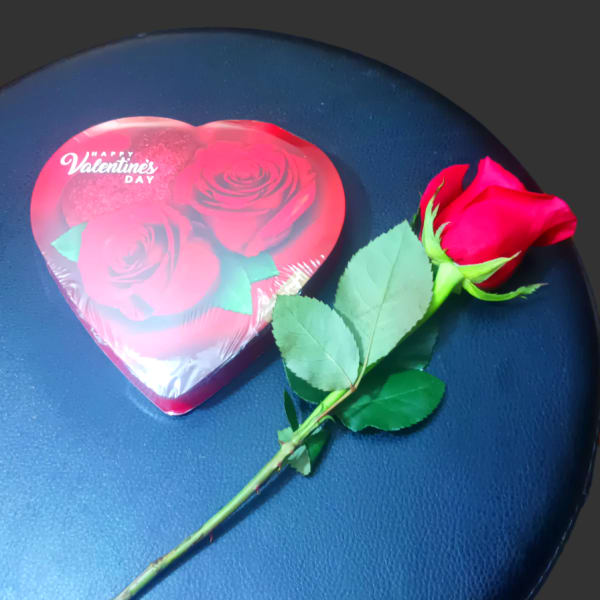 Single red rose beside a heart-shaped Valentine candy box