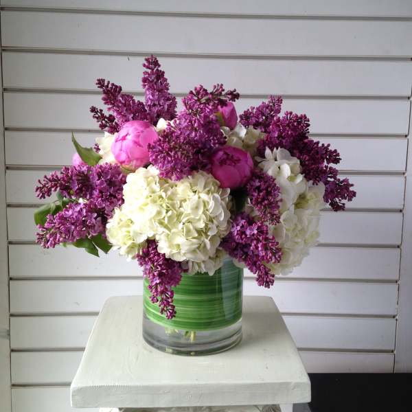 Pink peonies and white hydrangeas in a glass vase with purple lilacs