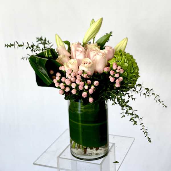 Pink roses and lilies arranged in a glass vase with green hydrangea