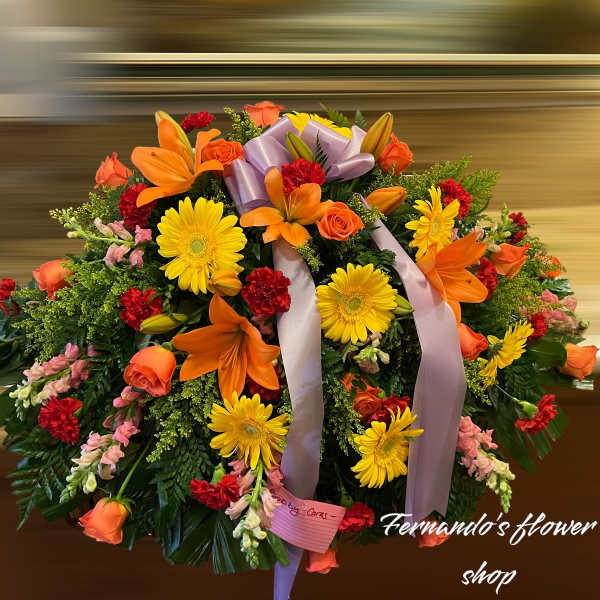 Large round spray of orange lilies, yellow gerberas, roses, and red carnations with a lavender bow.