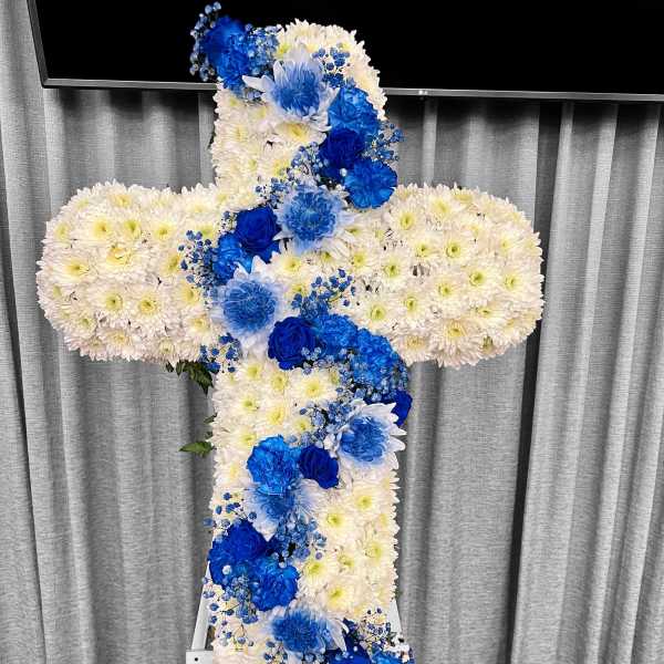 Standing cross of white flowers with cascading blue roses and blooms on an easel