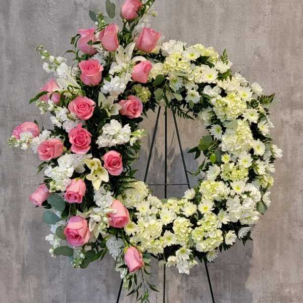 Standing wreath of white flowers with cascading pink roses on a metal easel