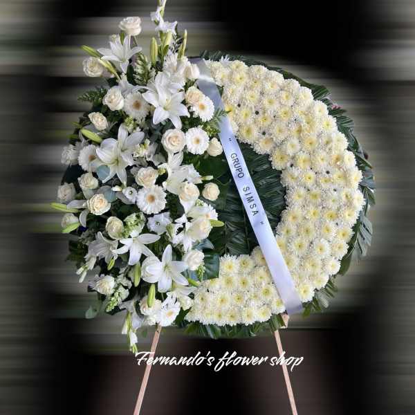 Standing white funeral wreath with lilies, roses, and chrysanthemums on an easel with a white ribbon