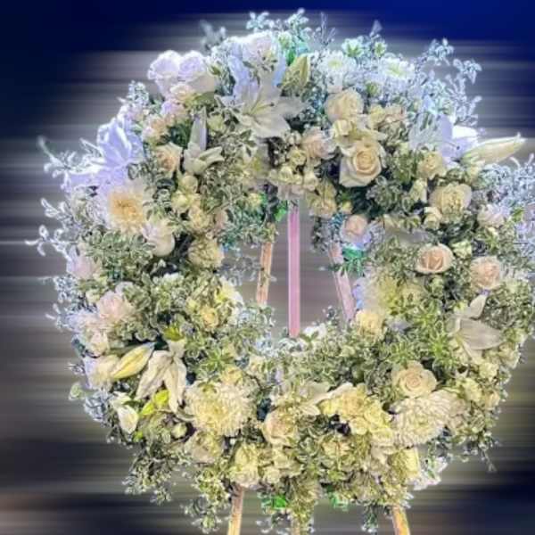 Large white floral wreath with roses and lilies displayed on a wooden easel