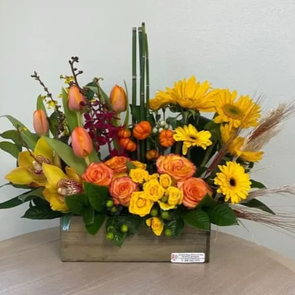 Mixed bouquet with yellow daisies, orange roses, and tulips in a wooden box
