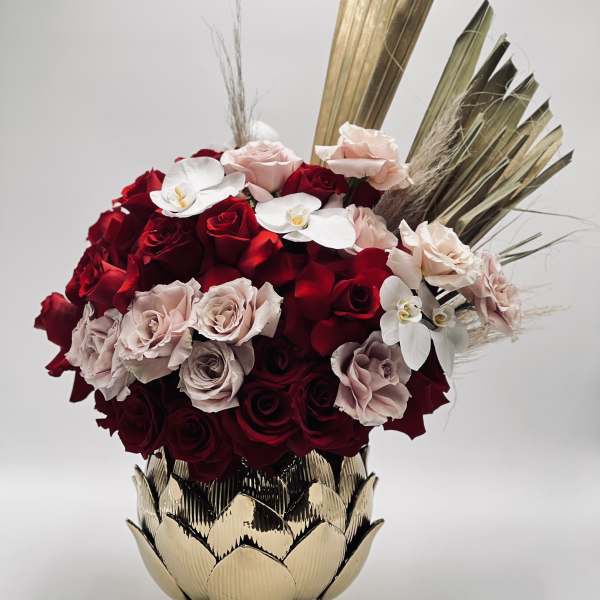 Red and blush roses arranged in a gold vase with white orchids
