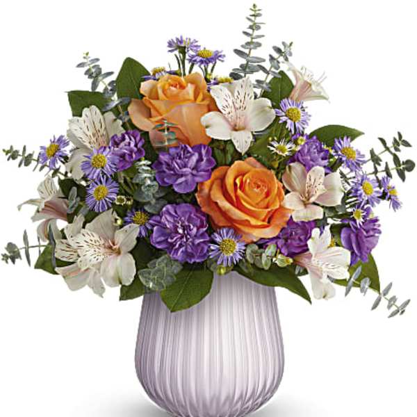 Bouquet of orange roses, purple daisies, and white lilies in a lavender vase