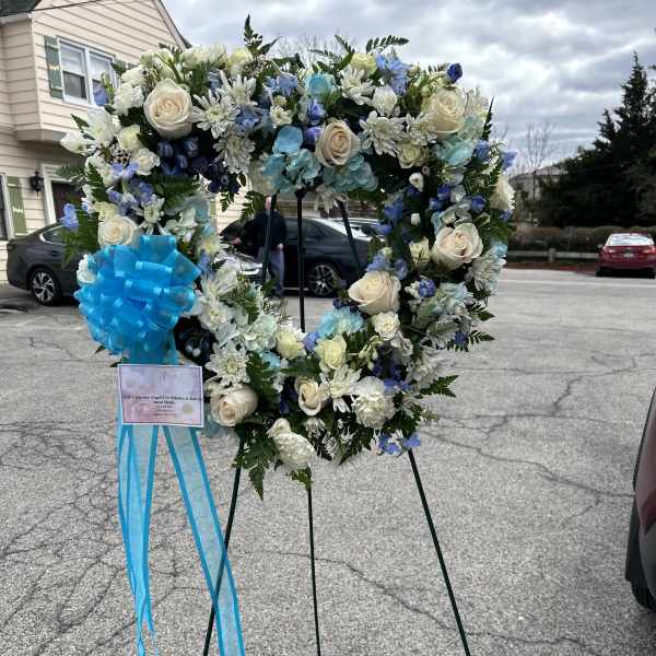 Heart-shaped funeral wreath with white and blue flowers on a stand