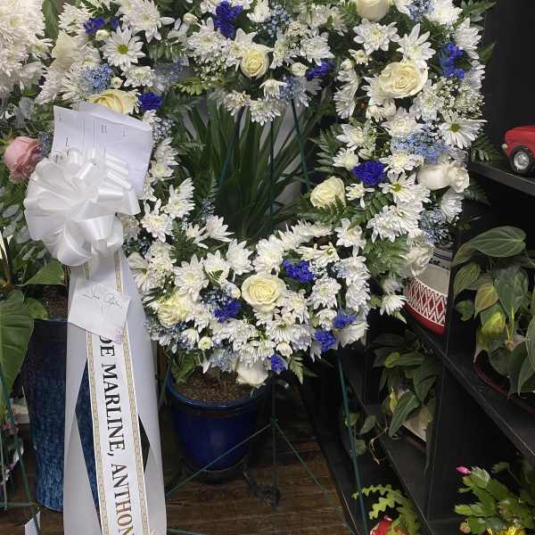 Large white floral wreath with cream roses and blue accents on an easel