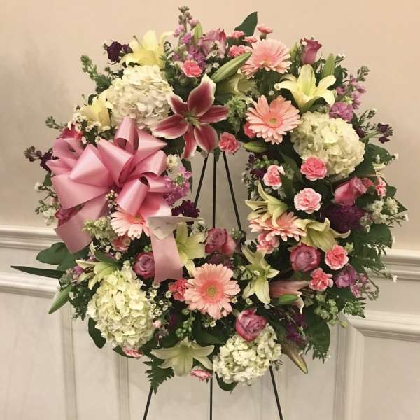 Heart-shaped floral wreath with pink ribbon and mixed pastel flowers on an easel