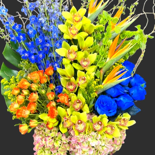 Colorful tropical bouquet in a tall glass vase with orchids and blue flowers