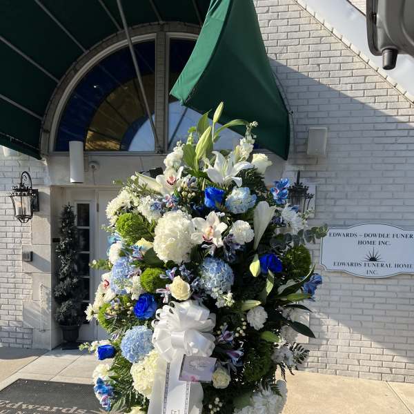Large funeral spray of white, blue, and green flowers on an easel