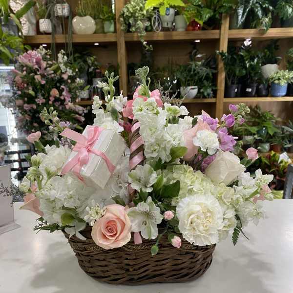 Basket arrangement of white and pink flowers with a small gift box and ribbon