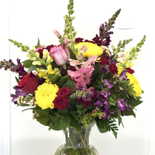 Mixed bouquet of roses, snapdragons, and chrysanthemums in a glass vase