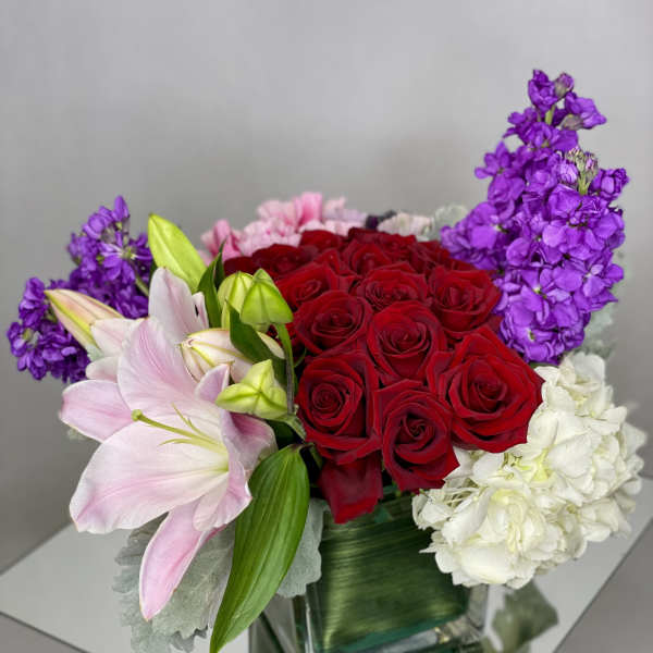 Bouquet of red roses, pink lilies, purple stock, and white hydrangea in a glass vase