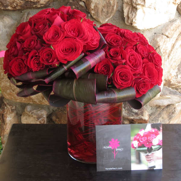 Red rose bouquet in a red glass vase with dark ribbon wrapping