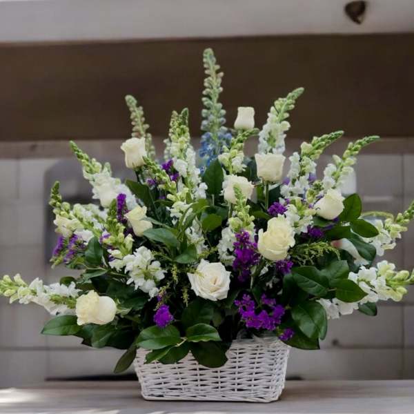 Tall basket arrangement of white roses and snapdragons with purple accents