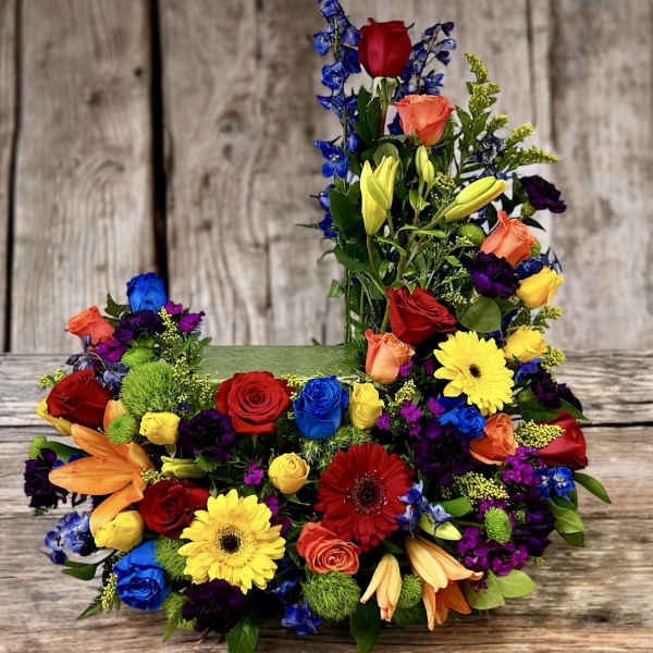 Tall and low arrangement of bright roses, lilies, gerbera daisies, and other blooms in a rectangular container.