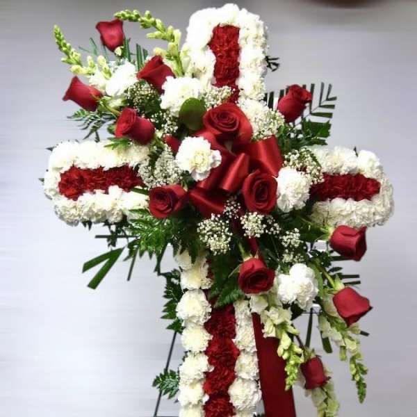 Tall red and white floral cross on an easel with red roses, carnations, and a satin ribbon