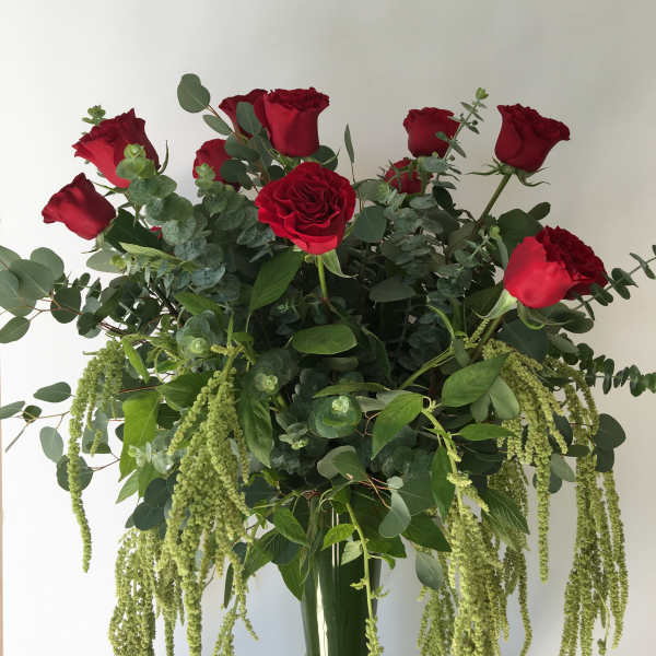 Tall bouquet of red roses with cascading green foliage in a glass vase