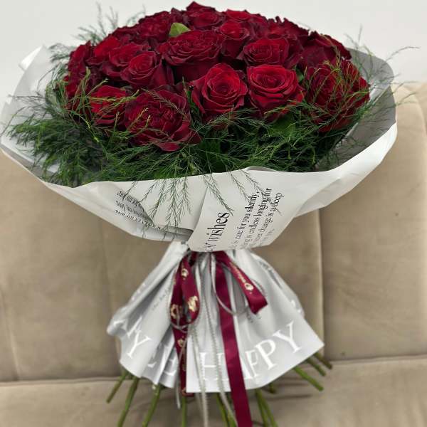 Bouquet of deep red roses wrapped in white paper with a ribbon