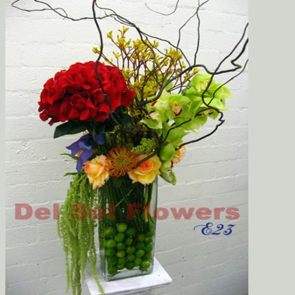 Tall floral arrangement with red and green blooms in a glass vase