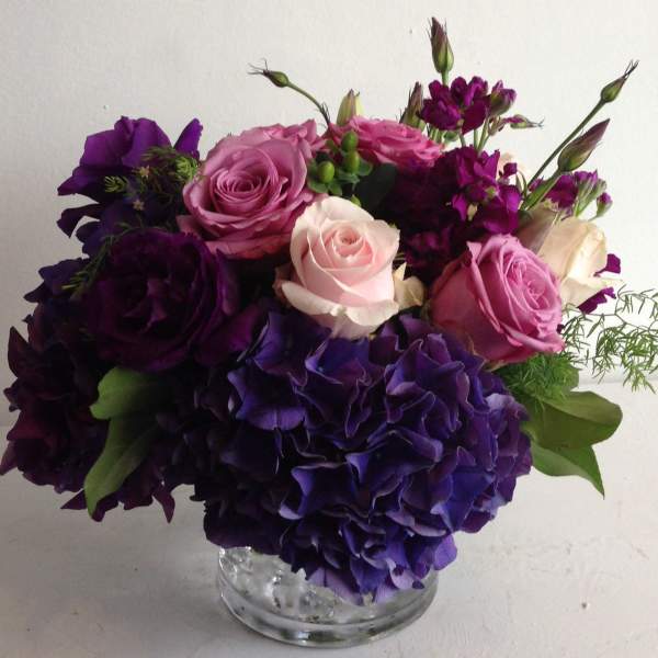 Purple and pink roses with hydrangeas in a clear glass vase