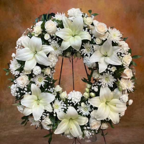 Standing wreath of white lilies, roses, and other white blooms on an easel stand