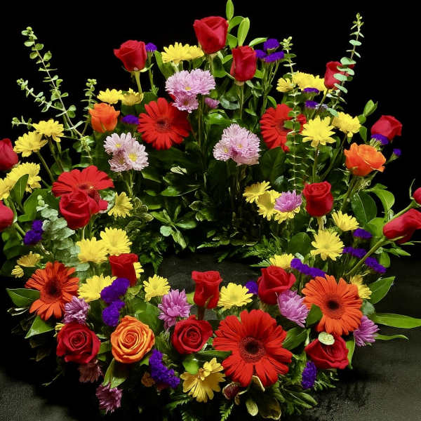Bright mixed flower wreath of roses, gerbera daisies, and mums in a circular design on a dark background