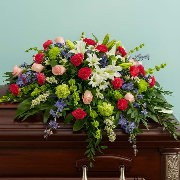 Large casket spray of red carnations, white lilies, pink roses, green blooms and blue delphinium