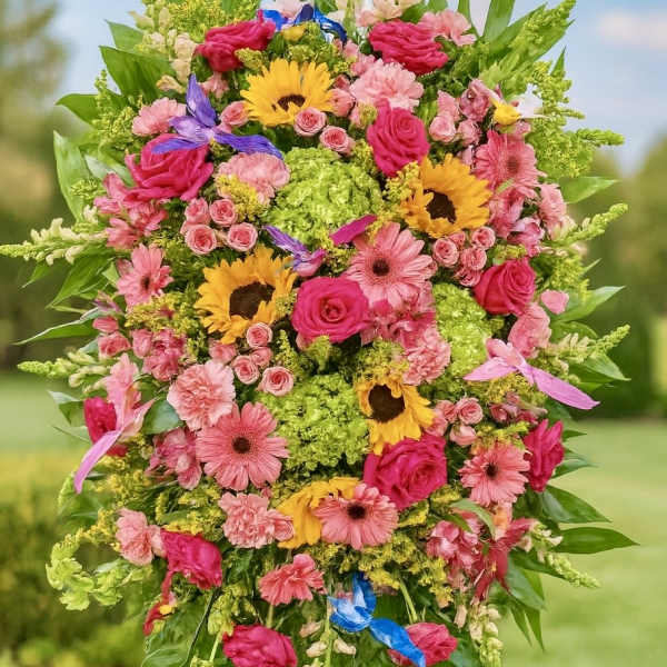 Tall standing spray of pink roses and gerberas with yellow sunflowers on a metal easel outdoors