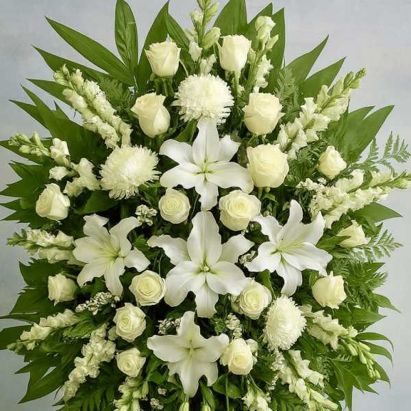 Standing spray of white lilies, roses, and other blooms with large green leaves on an easel