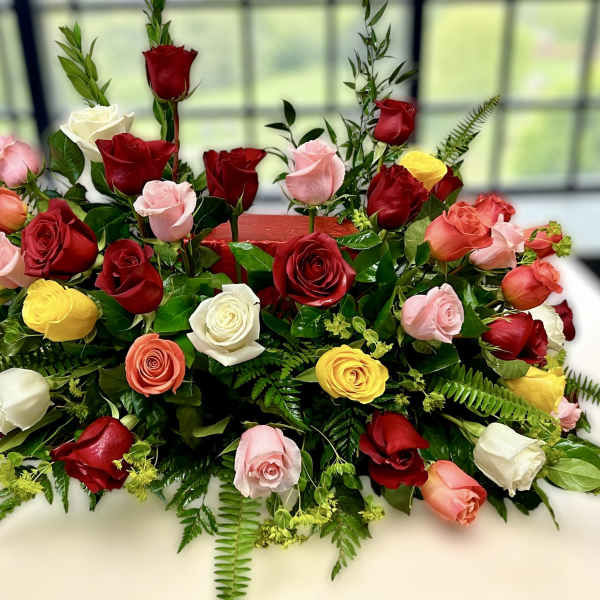 Low centerpiece of red, pink, yellow, and white roses arranged in a long, lush spray