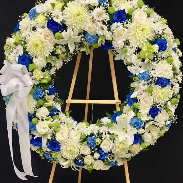 Large standing wreath of white and blue flowers with a white ribbon bow on a wooden easel